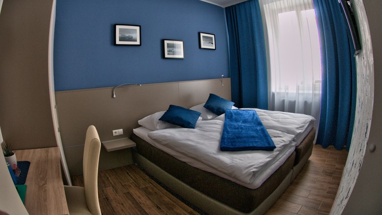 Modern guest room with blue accent, double bed and desk.