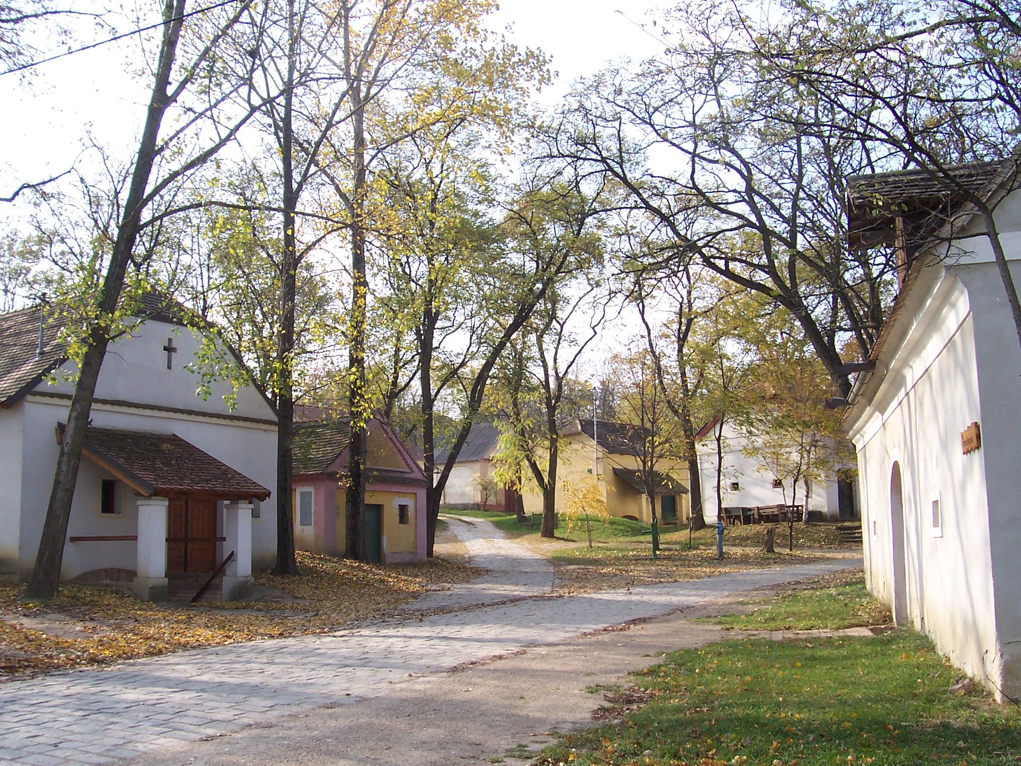 A quiet village square with small, traditional buildings and trees in the fall.