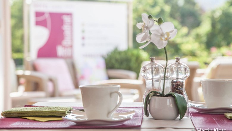 A laid table with two cups, salt and pepper shakers and a white orchid in the foreground.