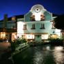 A traditional inn with a blue façade and illuminated windows at night, with a fountain in the foreground.