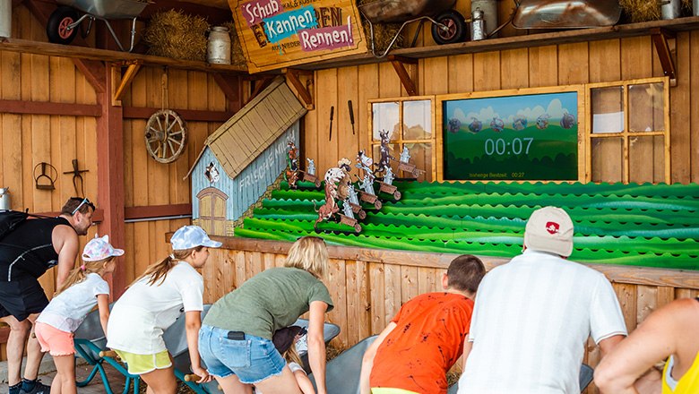 Children and adults in front of the "wheelbarrow race" attraction in an adventure park.