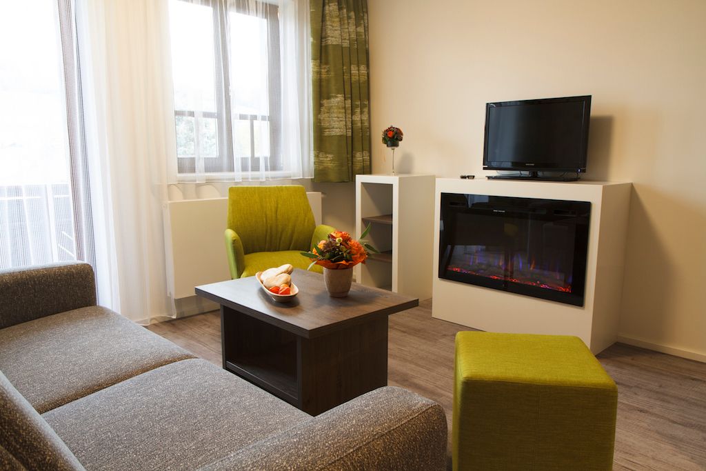 Modern living area with sofa, green armchair, coffee table, fireplace and TV.