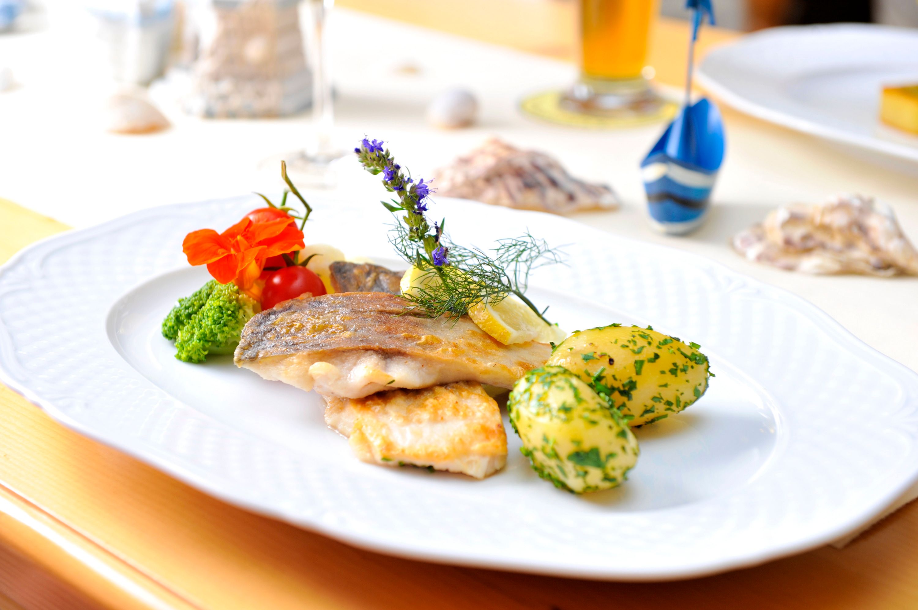 A plate of fried fish fillet, potatoes and vegetables, decorated with herbs and flowers.
