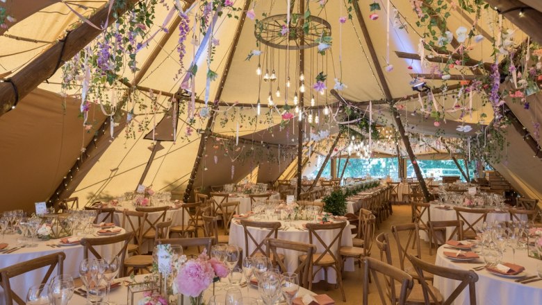 Interior view of a festively decorated tipi with round tables and flowers.