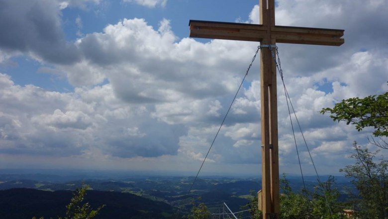 Summit cross on the Burgsteinmauer viewing mountain with a view of the cloudy sky and landscape.