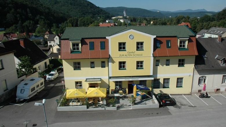 Hotel Zur Alten Schule, © Viregro Capital Gmbh Yellow building with the inscription 'Gasthof Zur Alten Schule', surrounded by hills and trees.