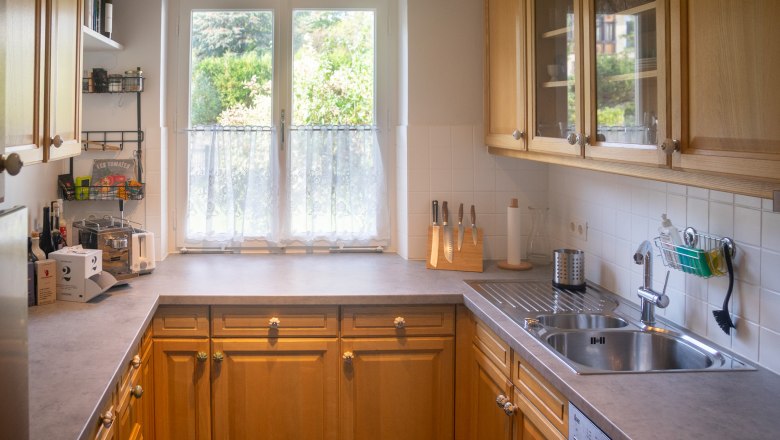 A bright kitchen with wooden cabinets, a window with a view of the greenery, a sink and work surfaces.