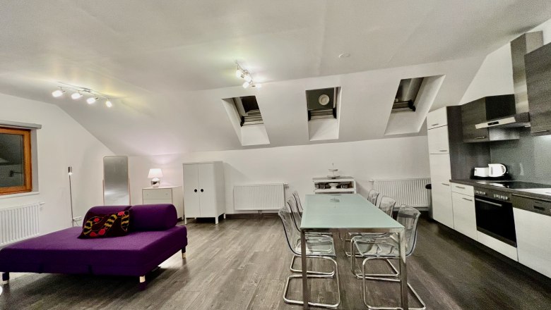 Modern loft with open kitchen, dining table and purple sofa.
