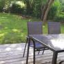 Terrace with table and chairs, surrounded by green garden.