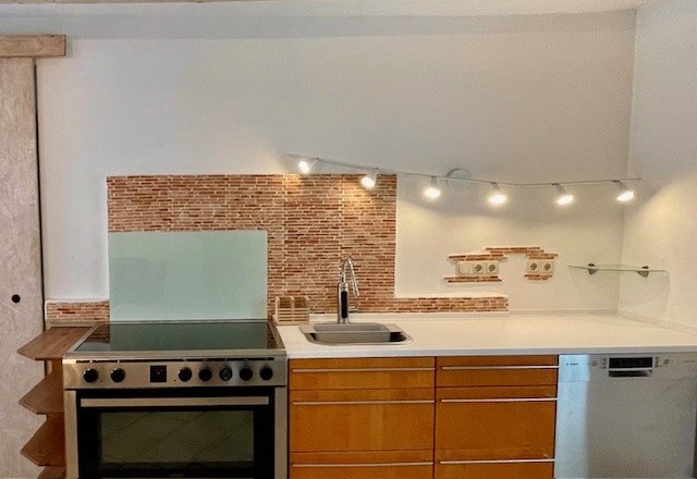 Modern kitchen with stove, sink and dishwasher in front of a mosaic tiled wall.