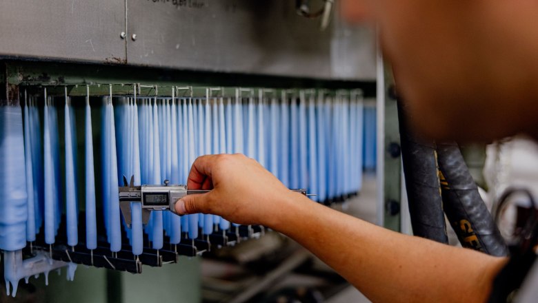 A person measures the thickness of blue candles with calipers in a factory.