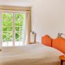 A bedroom with an orange headboard, a double bed and a window with a view of green trees.