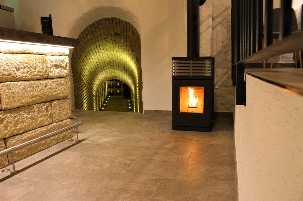 A wine cellar with an illuminated vaulted corridor and a burning fireplace.