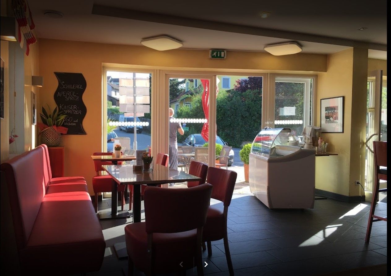 Interior of a bakery with red benches and tables, large windows and an ice cream counter.