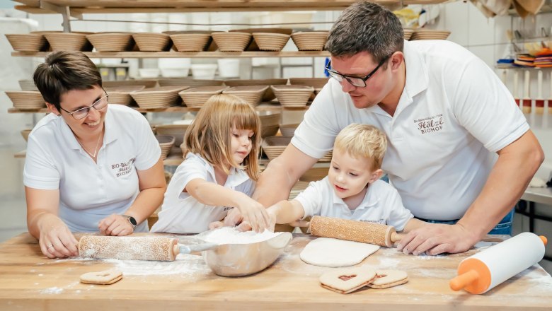 Family baking in a bakery with many bread baskets in the background.
