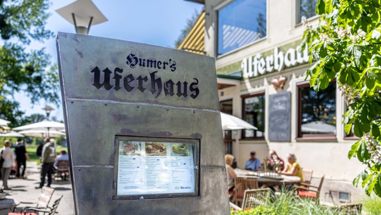 Exterior view of Humer's Uferhaus with menu in the foreground and guests in the background.