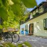 An idyllic country house with green shutters, bicycles and sun loungers in the garden, surrounded by trees.