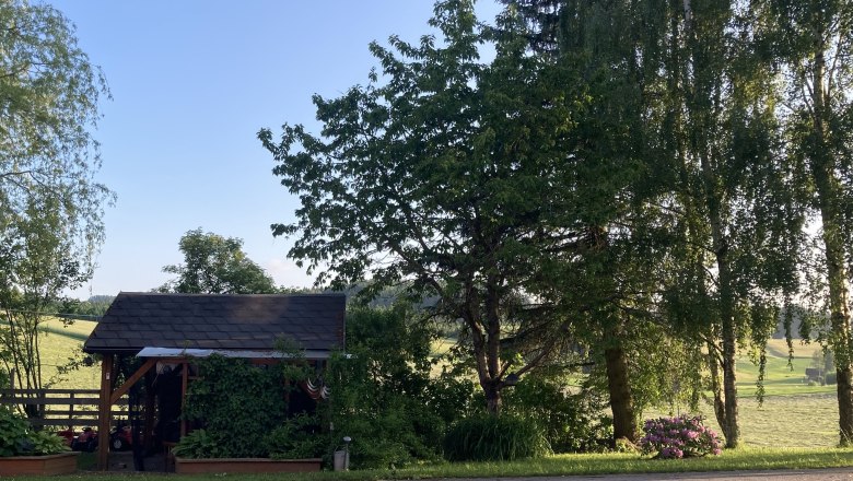 A small garden house surrounded by trees and plants, with a clear blue sky in the background.