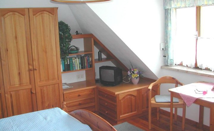 Cozy guest room with wooden furniture, a small TV, a table with chair and a window with curtains.