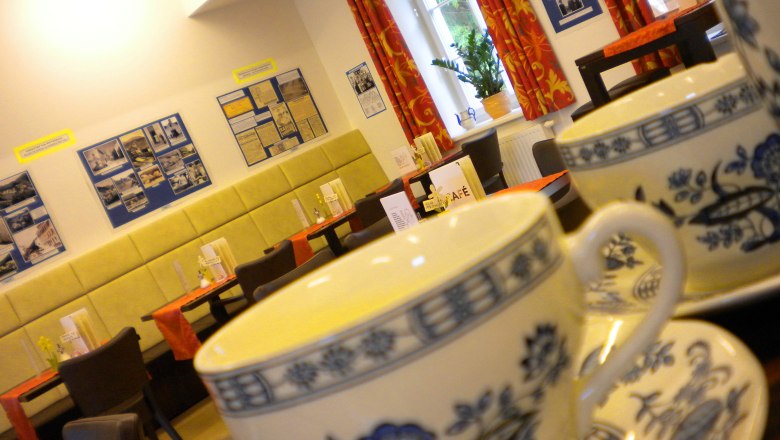 Interior view of a café with teacups in the foreground and decorated walls in the background.