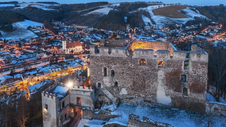 Kirchschlag castle ruins at dusk with illuminated town in the background.