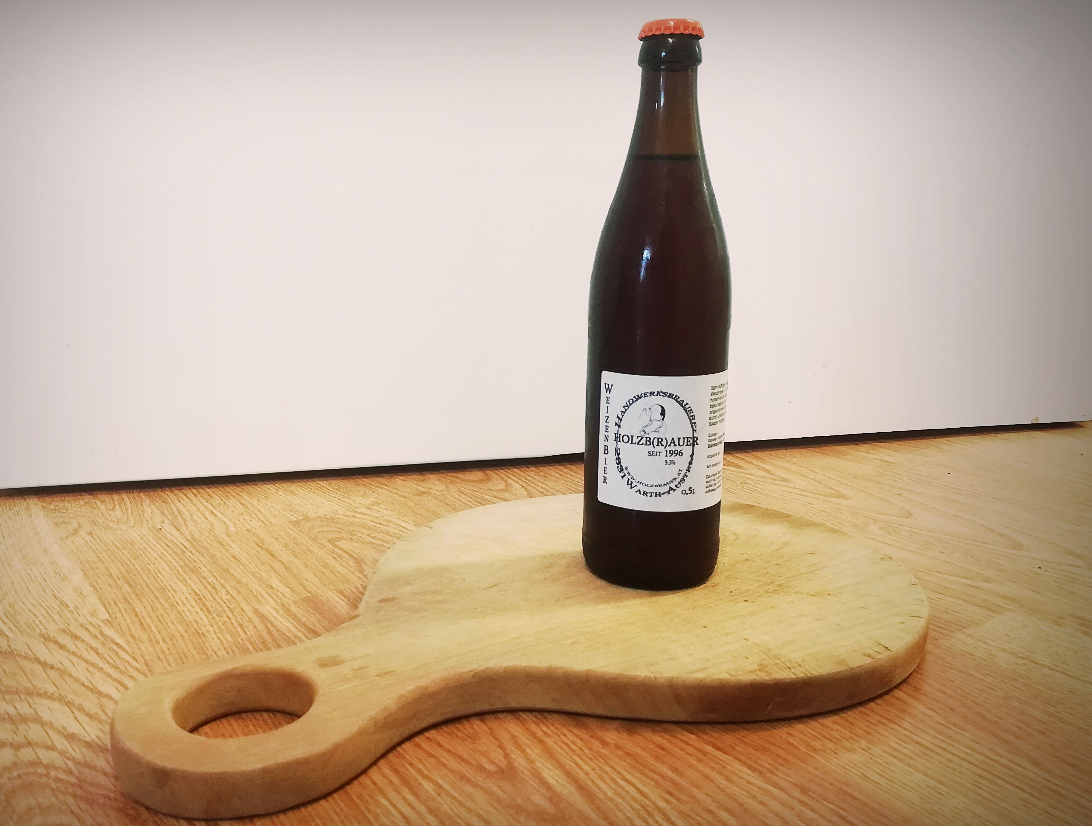 A bottle of wheat beer from Holzbräu stands on a round wooden board with a handle.