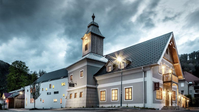 Hotel zum Glockenturm, © www.croce.at A hotel with a bell tower under a cloudy sky, illuminated by streetlights.