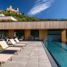 Modern hotel with pool and sun loungers, castle in the background.