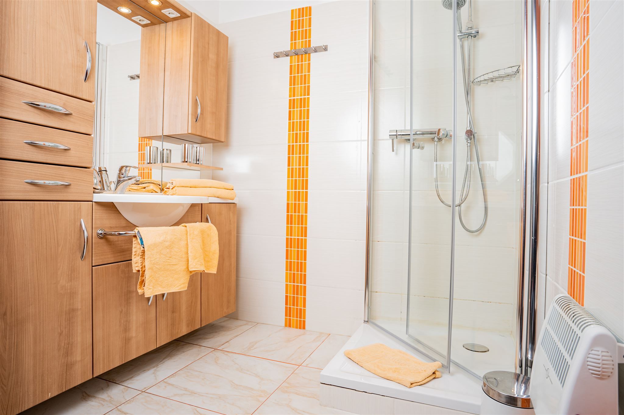 Modern bathroom with wooden furniture, shower and orange accents.