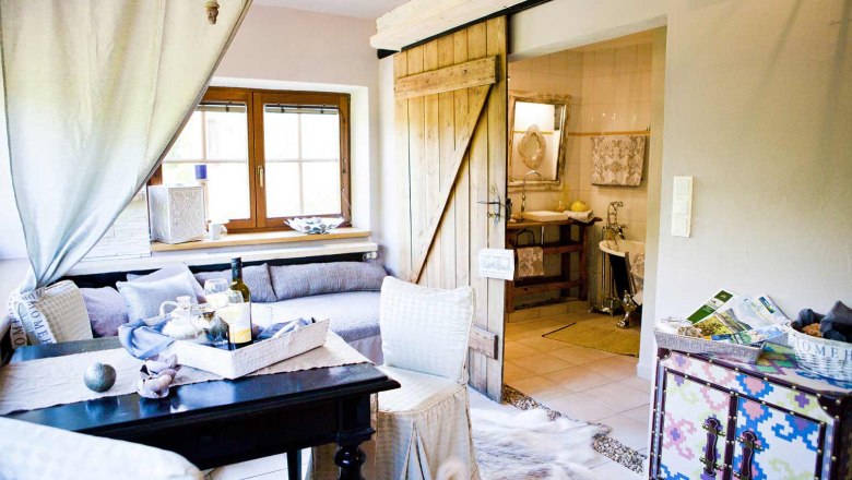 Cozy living room with wooden door, sofa, table and decorative elements, view into the bathroom.