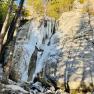 A frozen waterfall in a rocky landscape with trees in the foreground.