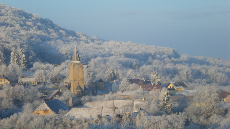 Winter landscape with village and church, surrounded by snow-covered trees.