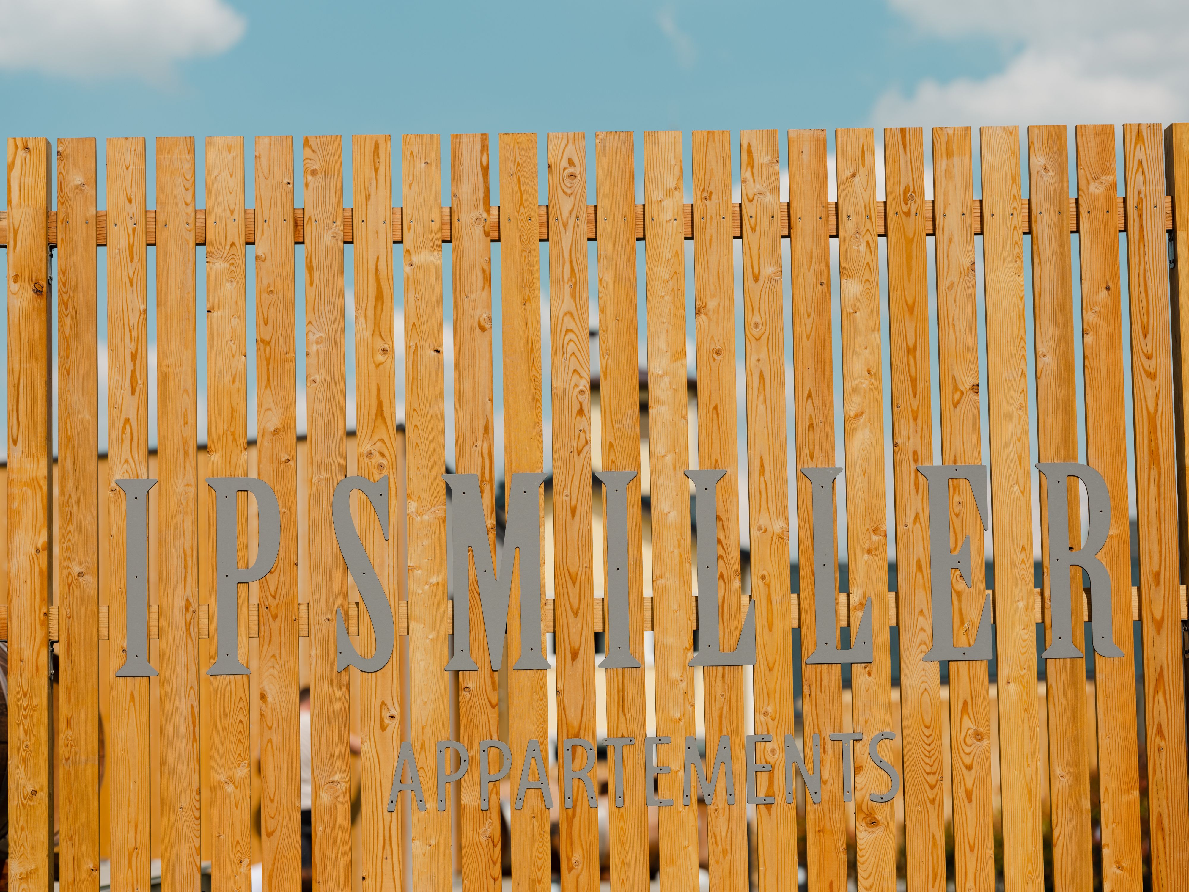 Wooden fence with lettering 'Ipsmiller Appartements'.