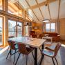 Interior view of a modern chalet with wooden walls, dining table and chairs, large windows and cozy seating area.
