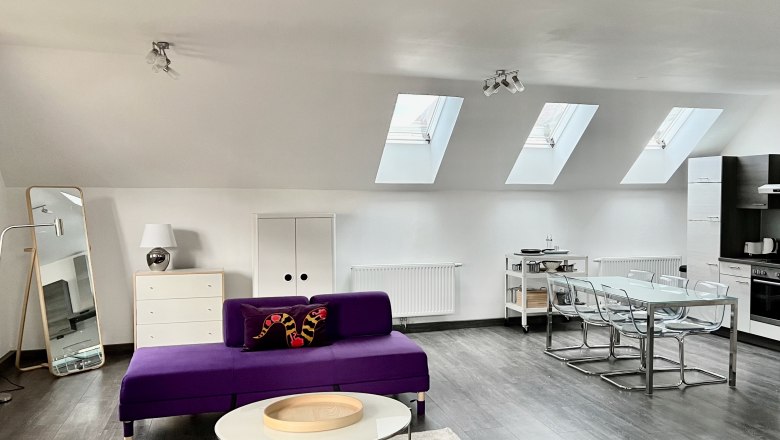 Modern loft with purple sofas, dining table and kitchenette under skylights.