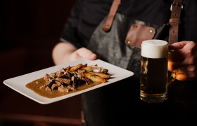 Person holding plate with meat dish and beer mug.