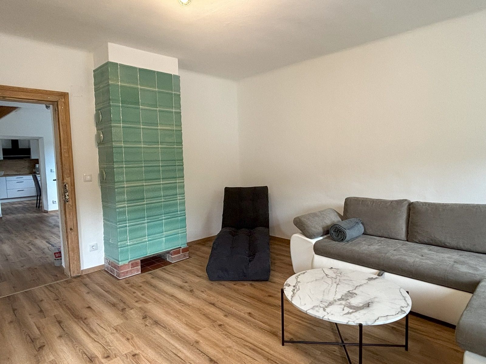 Living room with gray sofa, round marble table and green tiled stove.
