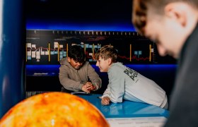 Two boys interact at a blue table in a science center.
