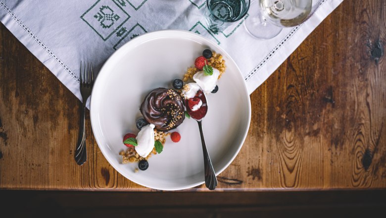 A dessert plate with a nougat tartlet, elderberry ice cream, berries and a spoon on a wooden table.
