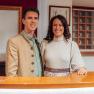 A man and a woman stand smiling behind a reception counter in traditional dress.
