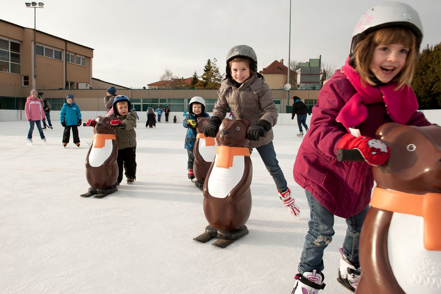 Children skating with penguin aids on an ice rink.