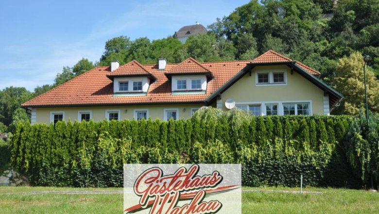 Exterior view of the Wachau guest house with red roof and green hedge.