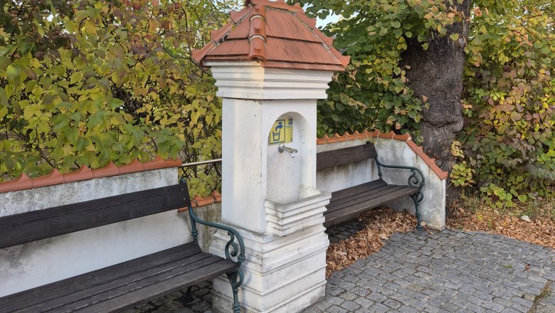 Two benches by a small fountain in an autumnal park.