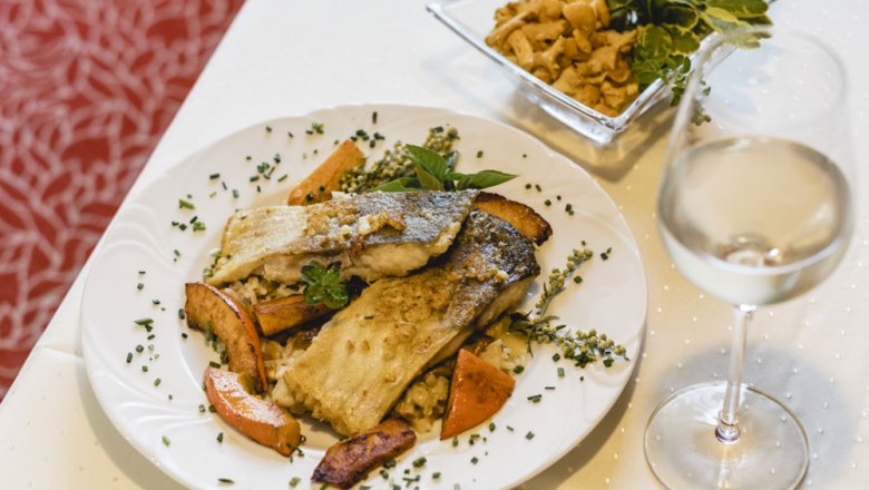 Gourmet dish with fish fillet, vegetables and white wine on a white table.