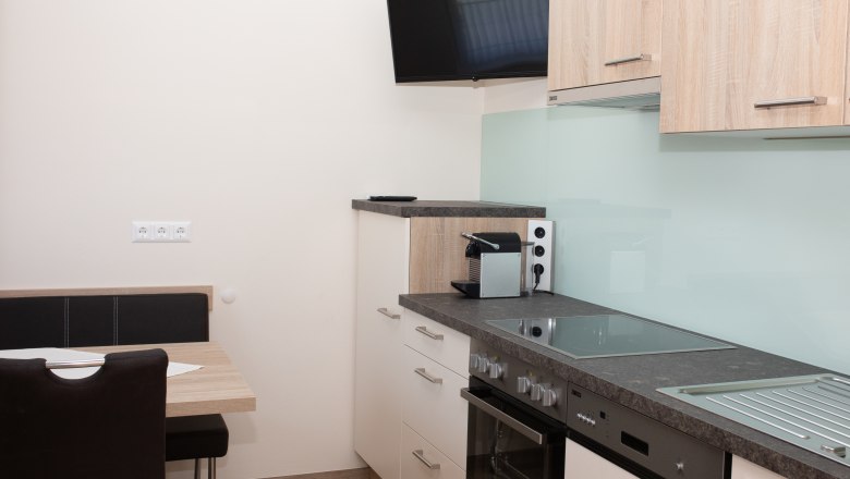 Modern kitchen with stove, sink, coffee machine and wall-mounted TV.