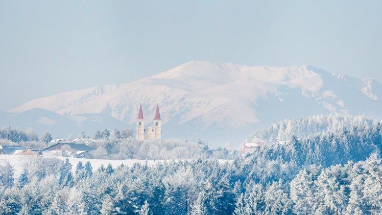Winter landscape with church and mountains in the background.