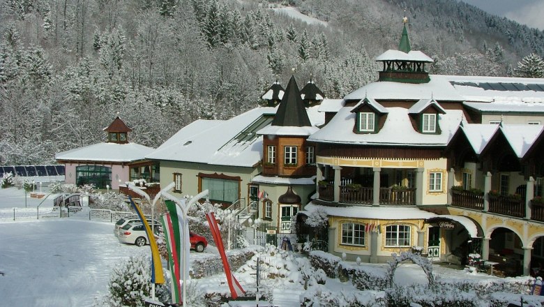 A snowy alpine-style hotel with towers and balconies, surrounded by snow-covered trees and hills.