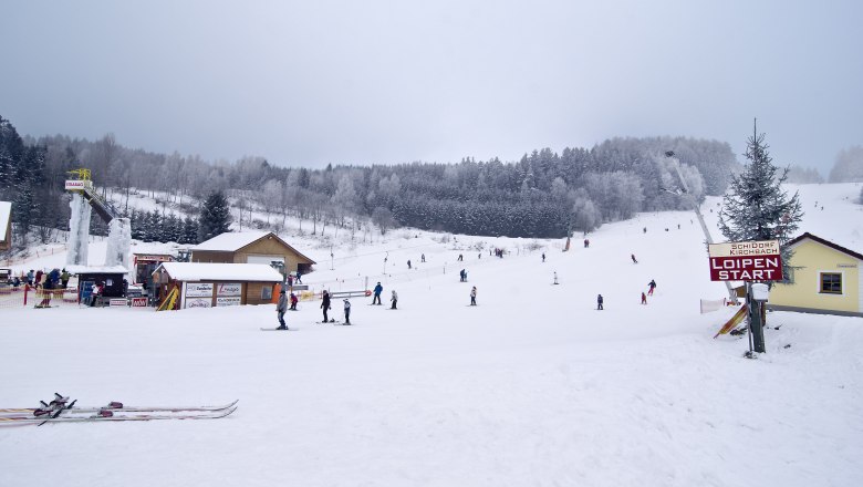Winter landscape with skiers in the ski village of Kirchbach, surrounded by snow-covered trees and hills.