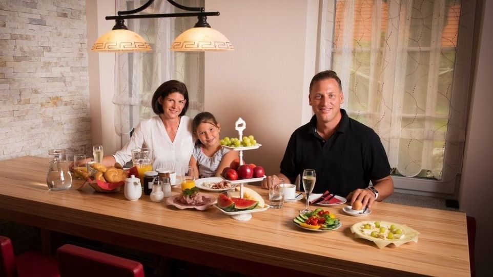 Family having breakfast at a wooden table with fruit and drinks.