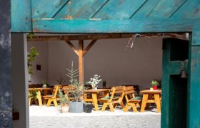View through an open gate onto an inner courtyard with wooden tables and plants.
